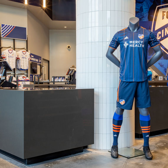 FC Cincinnati TQL Stadium gift shop with dark gray quartz counters, column covered in white tile, behind mannequin wearing the teams uniform.