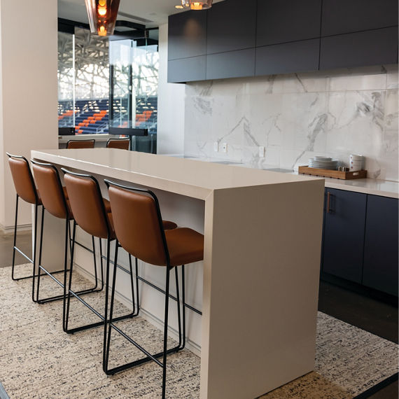 FC Cincinnati TQL Stadium suite with tan quartz island waterfall countertop, brown leather and black metal bar stools, and pendant lighting.