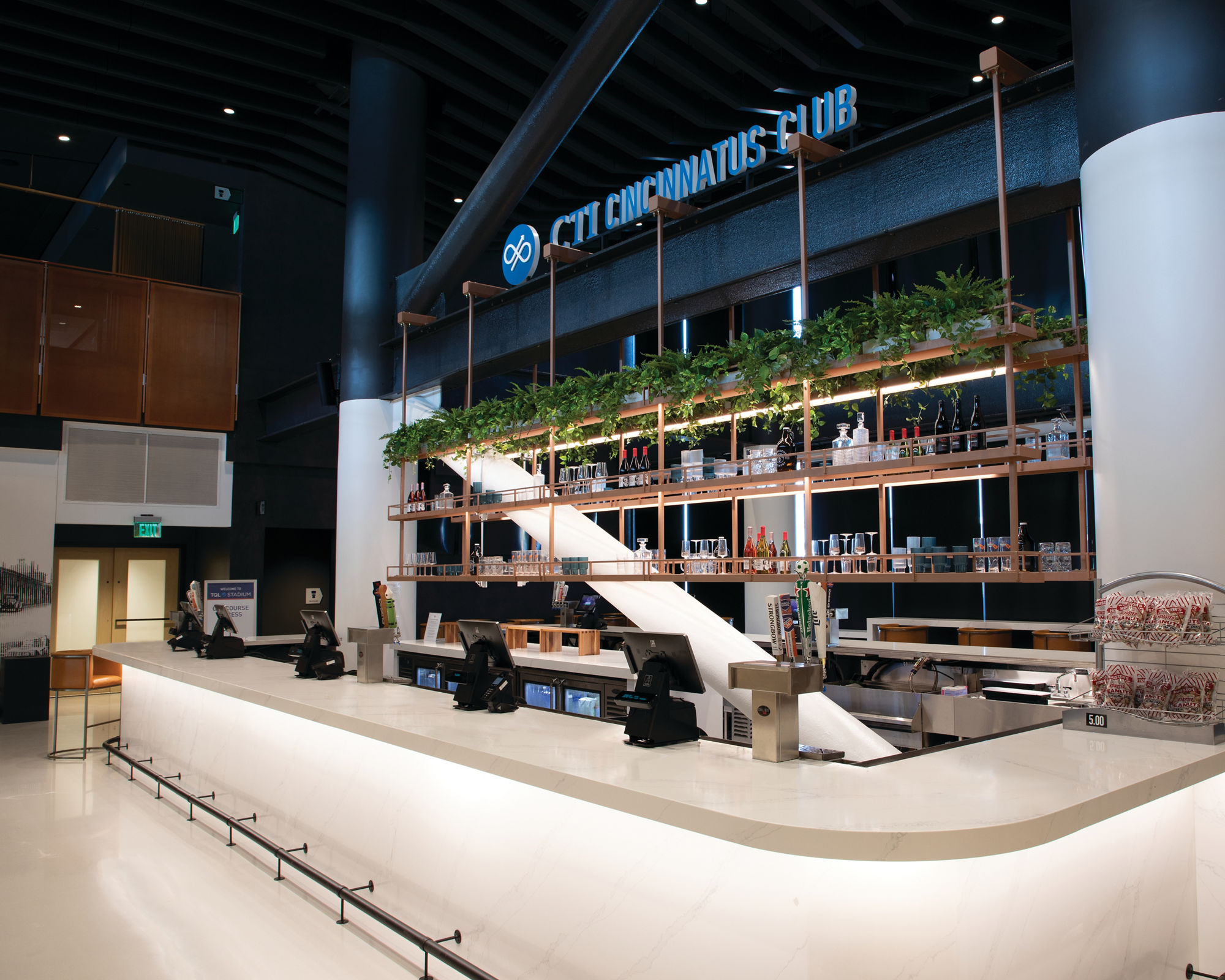 FC Cincinnati TQL Stadium club bar with base and countertop made of marble look white quartz with gray veining, shelves holding bottles and glasses.