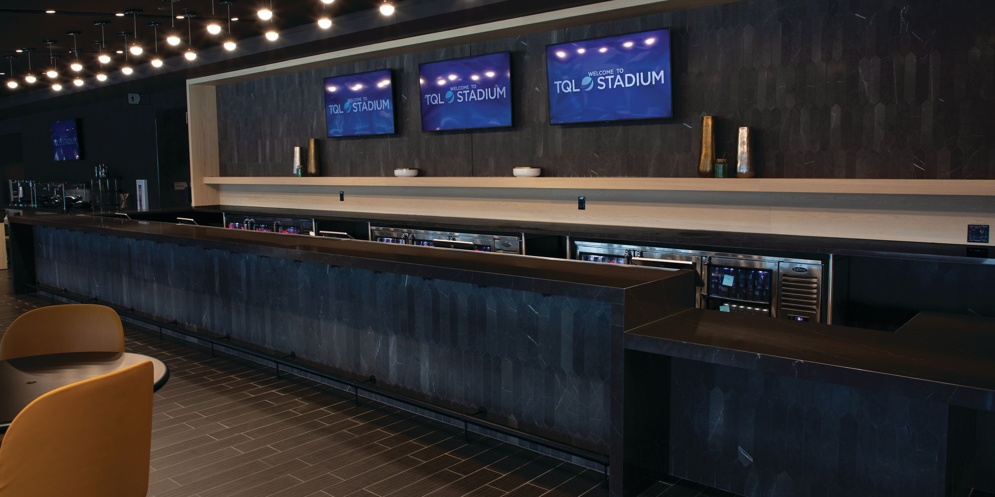 FC Cincinnati TQL Stadium club bar with black marble base and backsplash, countertop made of marble look black quartz with white veining, and TV monitors on back wall.