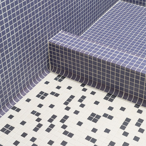 Close up of shower floor with purple square mosaic on floor and white and black square mosaic on bathroom floor. 