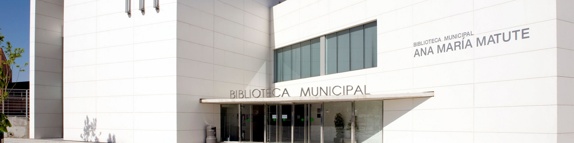 Library building with white monochromatic look rectangle porcelain slabs on walls, gray cement ground, and glass doors to enter building.