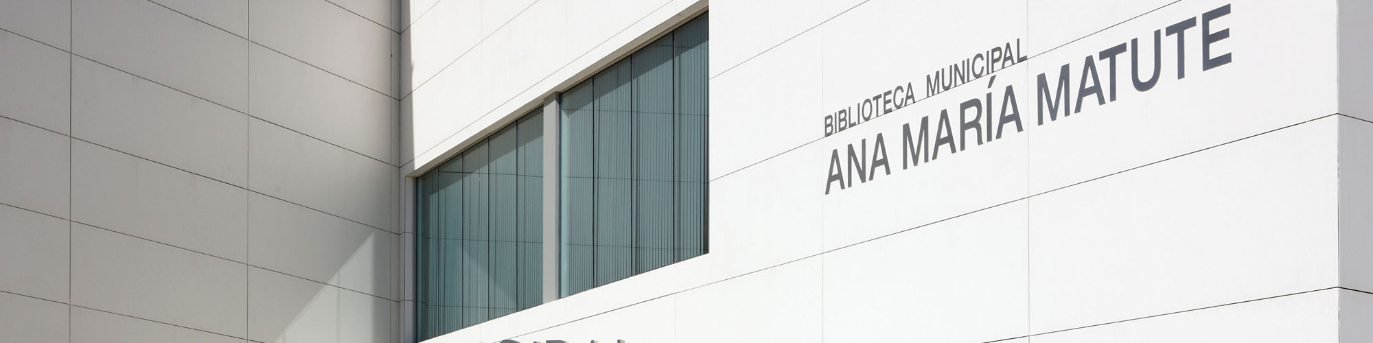 Library building with white monochromatic look rectangle porcelain slabs on walls, gray cement ground, and glass doors to enter building.