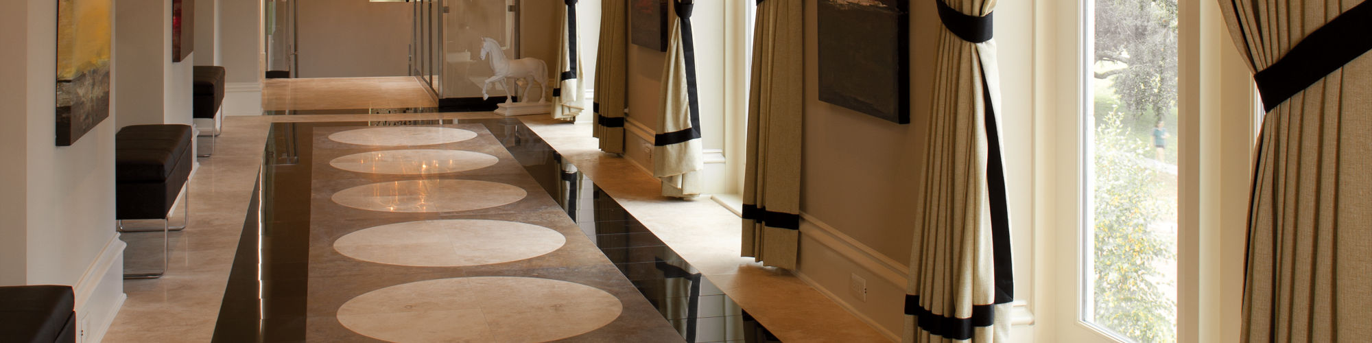 Hallway with black granite square floor tile lining gray and white floor tile, beige walls, and white horse stature at end of hallway.