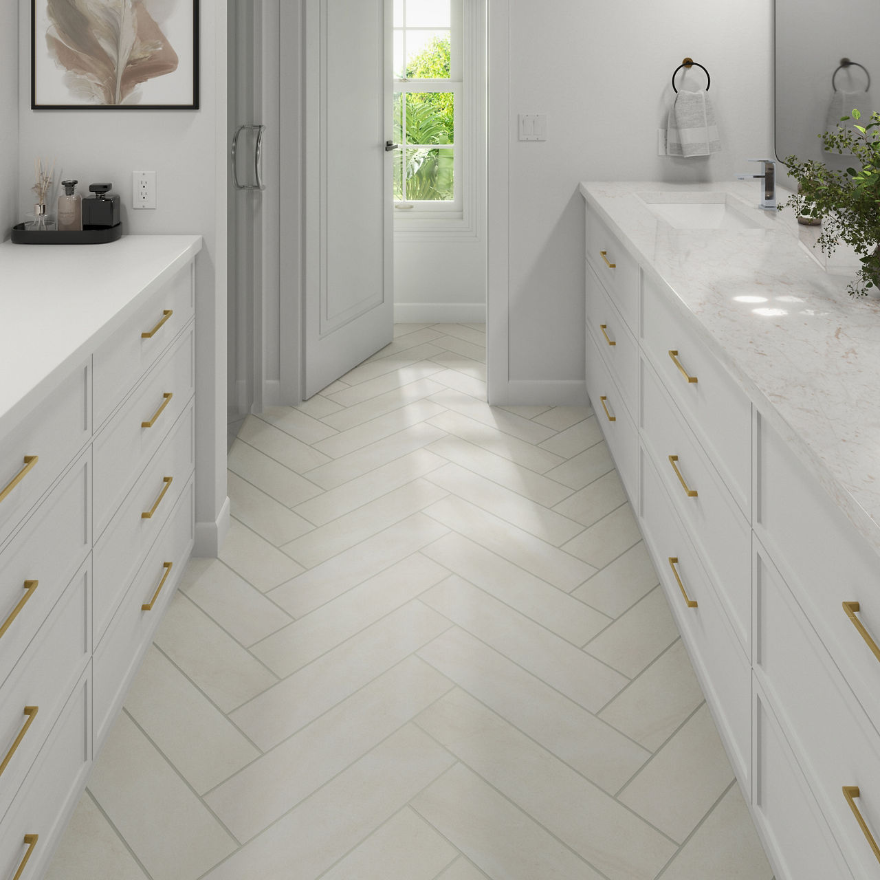 A bright, modern bathroom features long white cabinets with gold handles on both sides of a narrow walkway. The floor is laid in a light herringbone tile pattern leading toward a sunlit window with greenery visible outside. A marble countertop with s