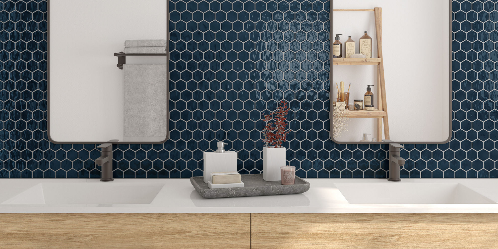 A contemporary bathroom features a double-sink vanity with light wood drawers and sleek hardware. Two rectangular mirrors are mounted above the sinks, set against a wall of dark blue hexagonal tiles. Minimalist lighting fixtures and organized toiletr