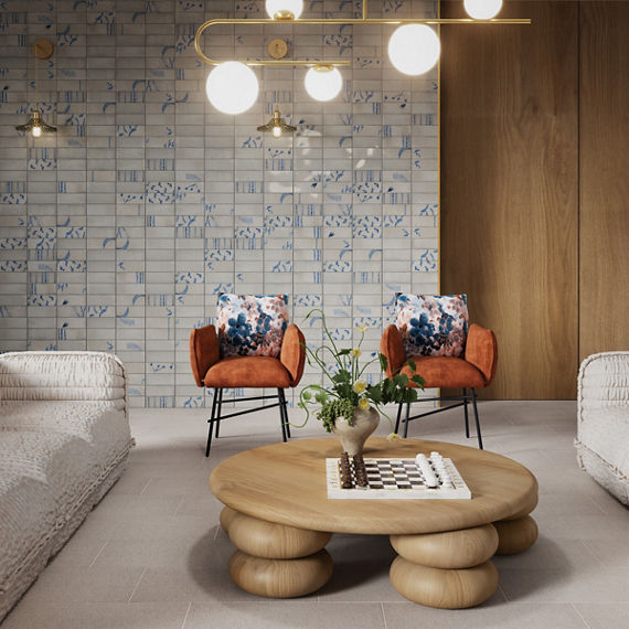 Waiting area with white and blue encaustic rectangle wall tile, wood side wall, beige fabric look rectangle floor tile, two white couches, wooden center table, and two orange chairs.