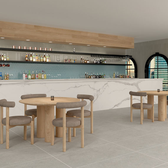 Restaurant bar with blue hexagon mosaic tile on backsplash, white marble look porcelain slab on counter, gray rectangle floor tile, and light wood tables and chairs.