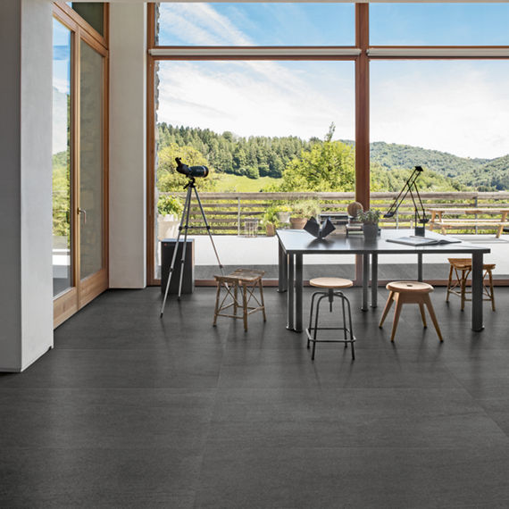 Dining room with gray stone look rectangle tile on floor,  table with books on it, stools, and floor to ceiling windows on walls showing mountain view.