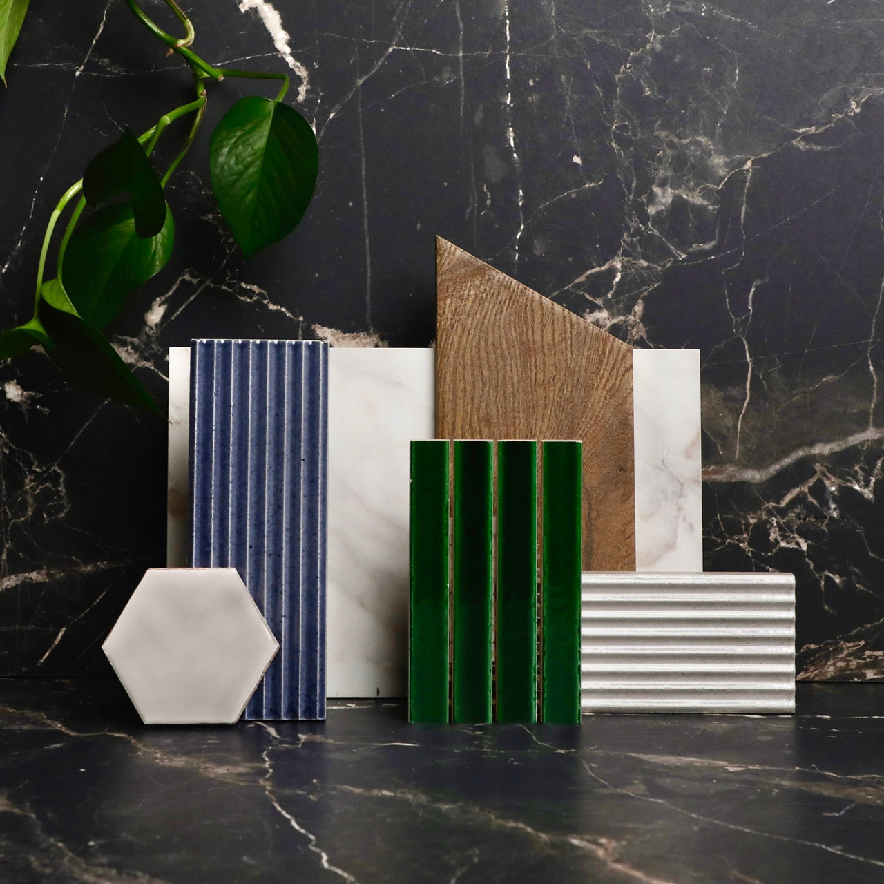This flatlay has black marble look rectangle tile, white marble look rectangle tile, wood look rectangle tile, gray marble look hexagon tile, white rectangle tile with linear design, green rectangle mosaic, and blue rectangle wall tile with linear design.