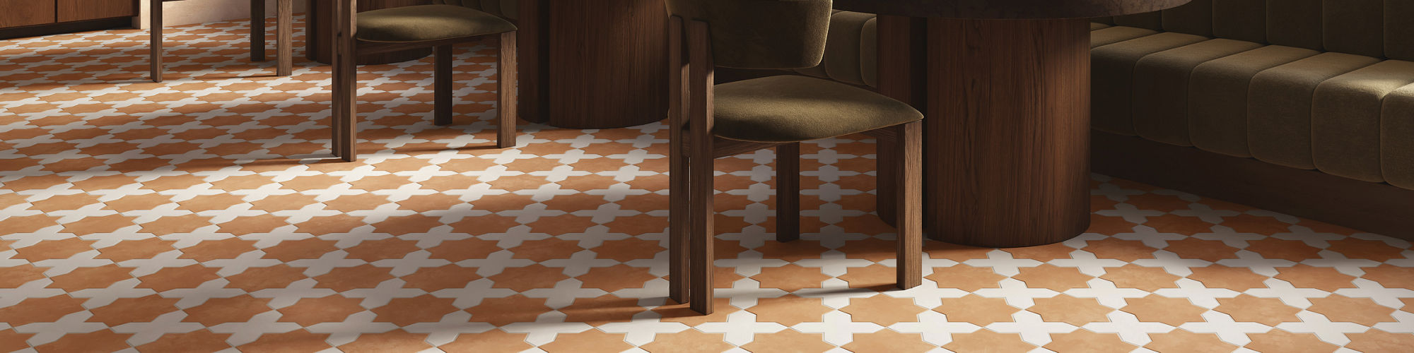 A contemporary restaurant interior features a striking geometric tile floor in warm terracotta and white tones. Round wooden tables with dark finishes are paired with cushioned chairs and a long green banquette along the wall. Large arched windows al