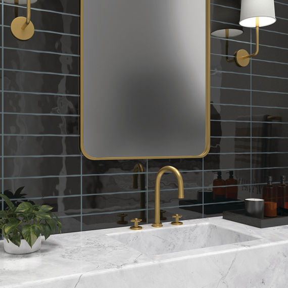 Bathroom with black undulated subway tile on back wall, white marble look countertop, and gold accents