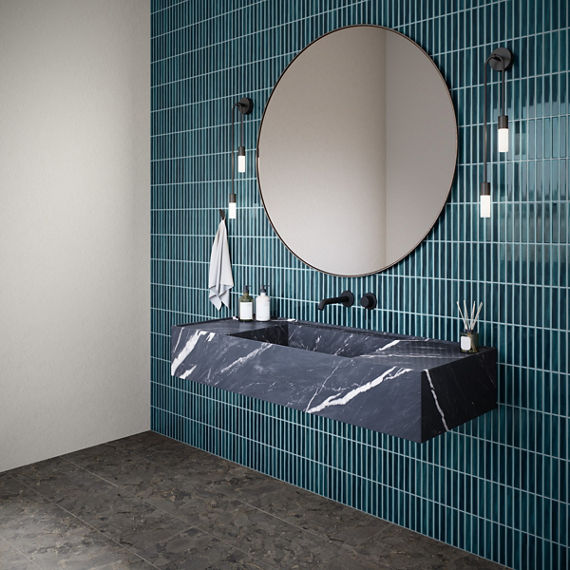 Bathroom with blue rectangle tile in vertical pattern, black stone look rectangle tile, black marble look sink, and round mirror above sink.