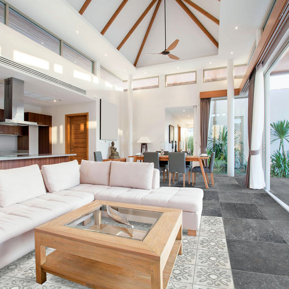 Living room with gray stone look rectangle tile on floor, white encaustic concrete look tile in middle creating tile rug, white couch, white walls, and wood accents.