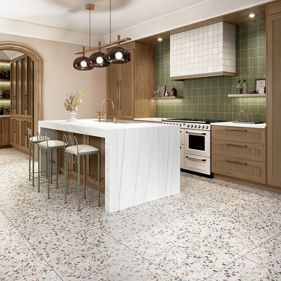 Kitchen with green square wall tile on back wall, white square tile on vent hood, white walls, wooden cabinets, white marble look countertops, and white terrazzo look square floor tile.