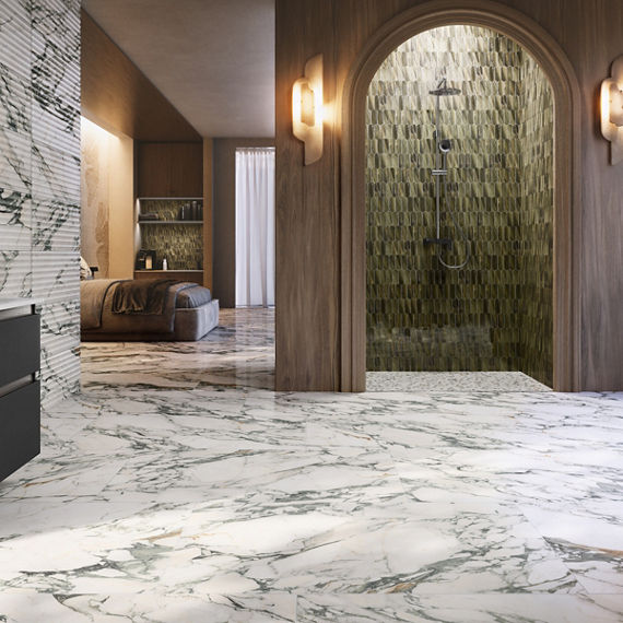 A contemporary bathroom features expansive white marble flooring with gray veining leading to an arched walk-in shower. The shower interior is clad in textured green tiles with a sleek wall-mounted showerhead and controls. Warm wooden wall panels and
