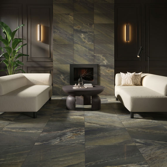 Contemporary living room interior featuring a sleek stone-tiled floor and matching fireplace surround. Two minimalist cream sofas face a low round coffee table in the center of the room. Vertical wall sconces cast warm light on dark paneled walls, en