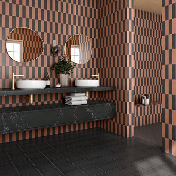 Bathroom with orange and black rectangle tile in vertical pattern on walls, black square tile on floor, and two white sinks on black marble look counter.