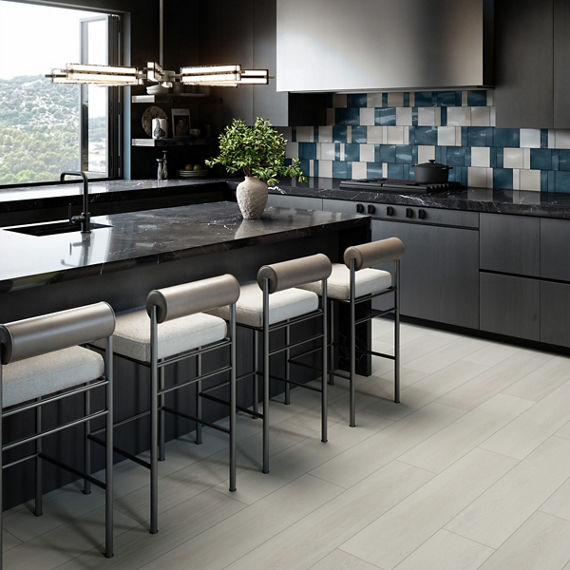 Kitchen with white and blue rectangle and square tile on backsplash, light wood floor tile, black cabinets, and black marble look countertop.