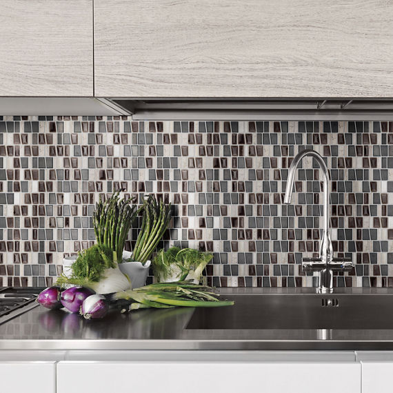 Kitchen with gray glass mosaic on backsplash, silver countertop, white cabinets, and vegetables on counter.