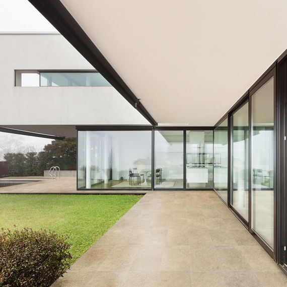 Backyard with beige stone look rectangle tile on edge of house, floor to ceiling glass windows, and white walls.