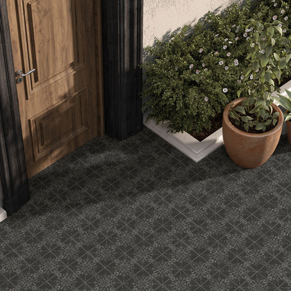 Close up of outdoor patio with gray square concrete look encaustic tile on floor, two plants in a pot, ladder, and greenery.