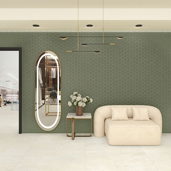 Waiting area with green hexagon mosaic tile on wall, white marble look rectangle floor tile, white couch, and oval mirror.