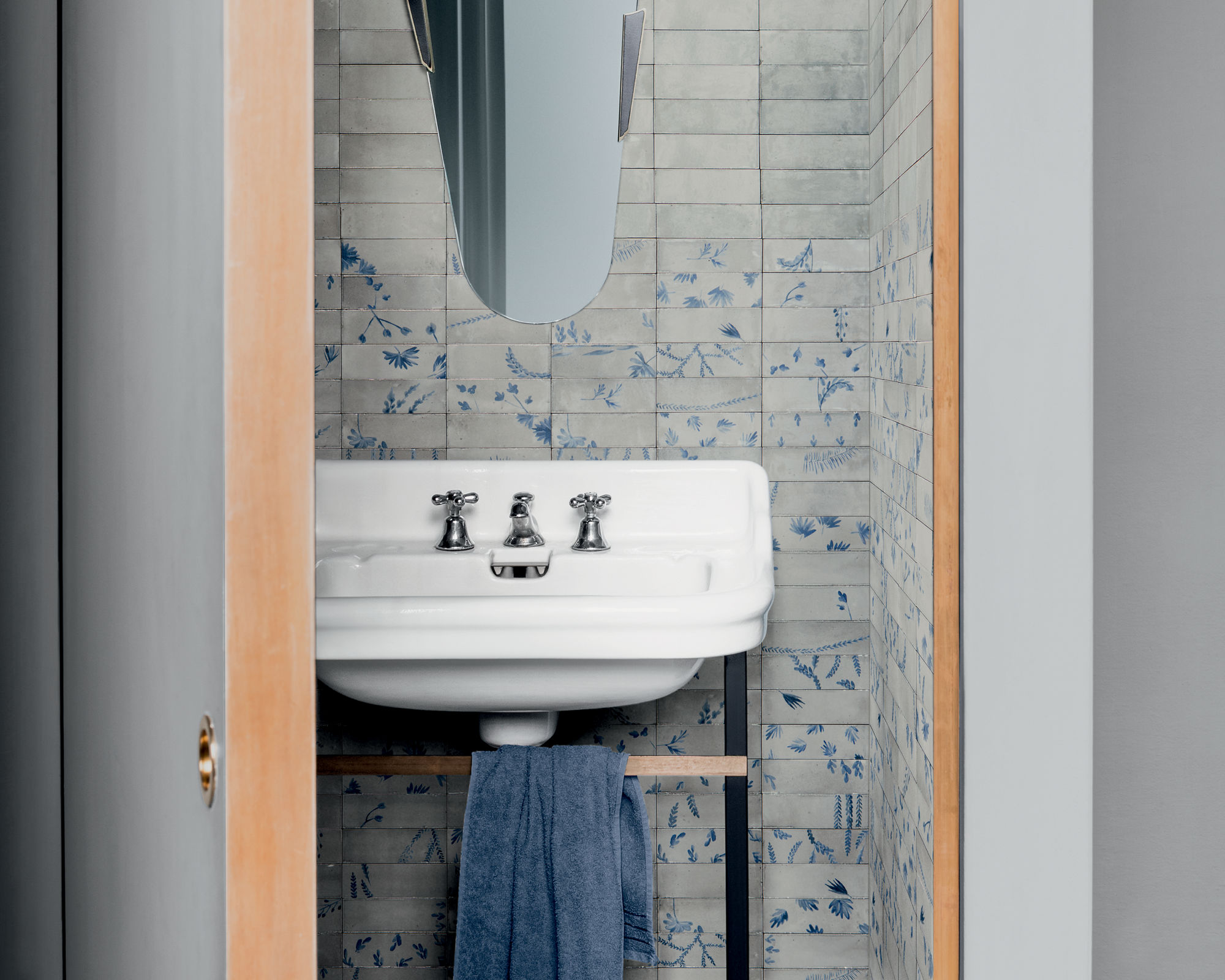 A contemporary bathroom features a white porcelain sink with chrome fixtures, set against a wall of gray and blue patterned tiles. 