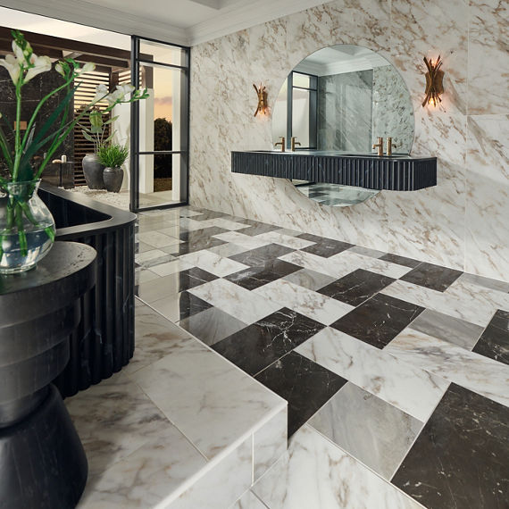 Bathroom with white marble look rectangle tile on wall and floors, black marble look rectangle tile on floor, black sink counter, black bathtub, and gold accents.