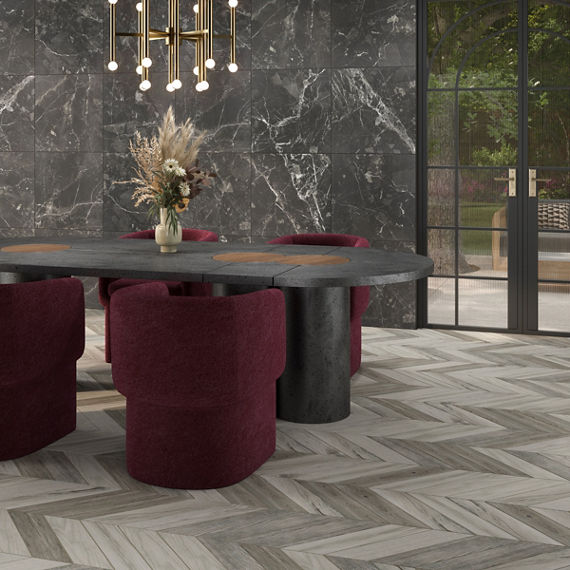 Dining room with light gray wood look floor tile in chevron pattern, gray marble look wall tile, black dining table, and red chairs.