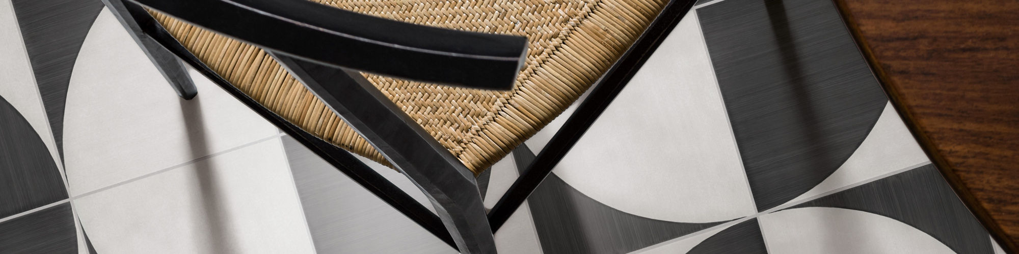 Overhead view of white and black concrete look encaustic tile, wooden table, and wicker chair.