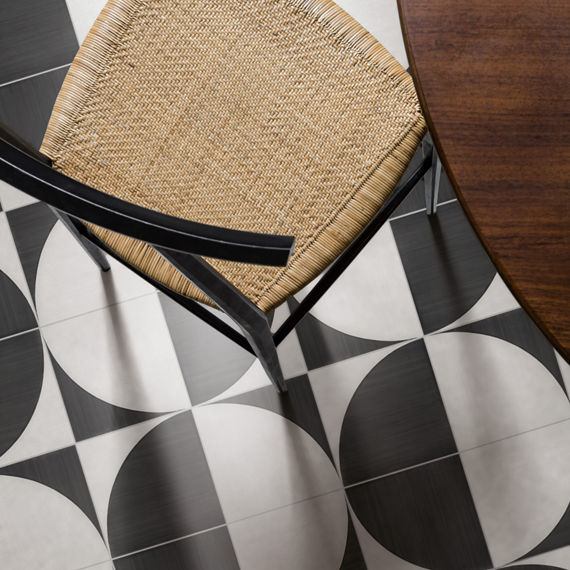 Overhead view of white and black concrete look encaustic tile, wooden table, and wicker chair.