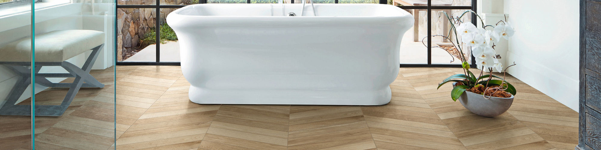 Bathroom with wood planks in chevron pattern, white tub, glass shower, and floor to ceiling windows.