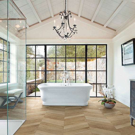 Bathroom with wood planks in chevron pattern, white tub, glass shower, and floor to ceiling windows.