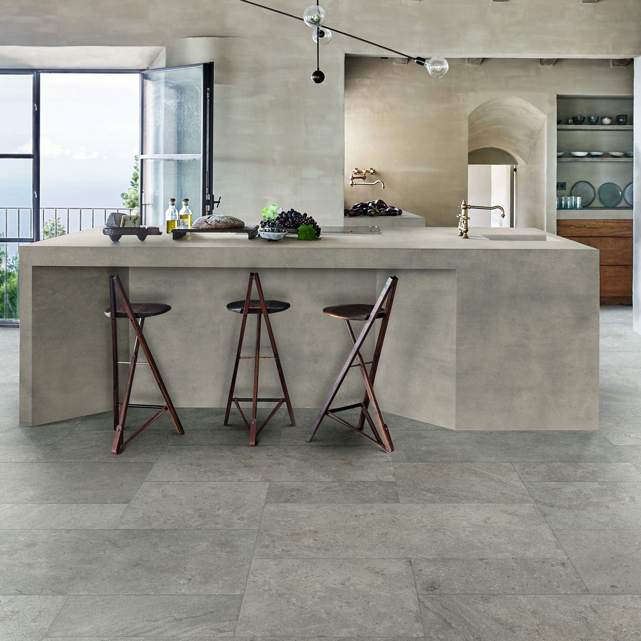 Kitchen with gray stone look square floor tile, gray counter and walls, and three bar chairs at counter.