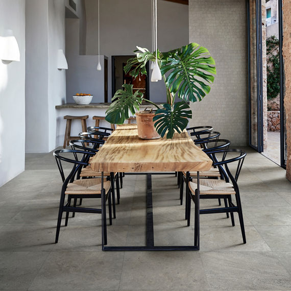 Dining room with gray stone look square floor tile, wood dining table, wood chairs, and plant on table.