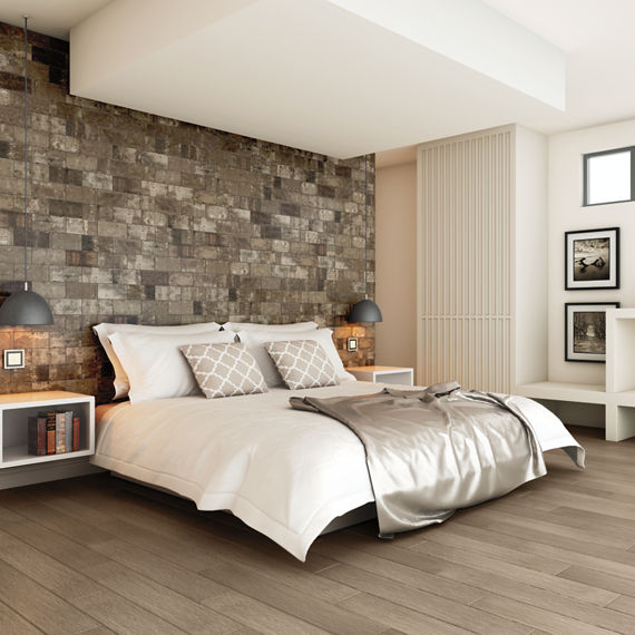Bedroom with gray stone look rectangle tile in brick joint pattern on back wall, white bed, white side walls, and wood floor.