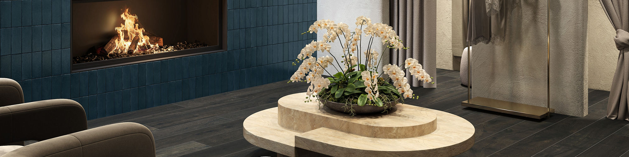 Fitting room waiting area with dark wood look floor tile, blue rectangle tile on side wall, fireplace, two gray chairs, and beige coffee table in center.