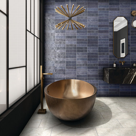 Bathroom with dark blue rectangle subway tile on back wall, white rectangle floor tile, black marble look counter, and copper tub.