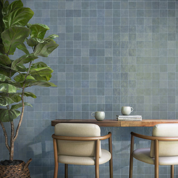 Dining area with light blue square wall tile, wooden table, two white chairs, and small tree on the side.