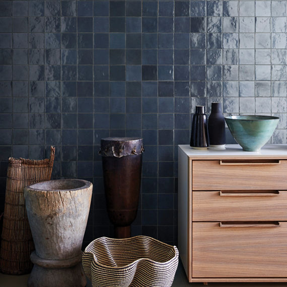 Bedroom with dark blue square tile on back wall, wooden dresser, various tall vases, and small vases on dresser.