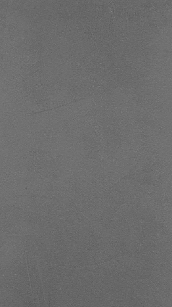 The image features a close-up view of a textured dark gray surface, resembling concrete or plaster. Subtle brush strokes and irregular patterns are visible, giving the surface a tactile, industrial feel. The overall tone is cool and monochromatic, wi