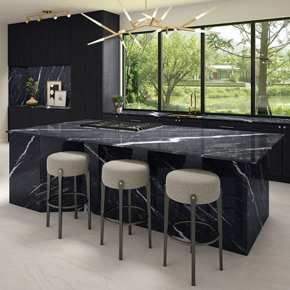 Kitchen with black marble look porcelain center island, white bar stools, and large windows showing greenery.