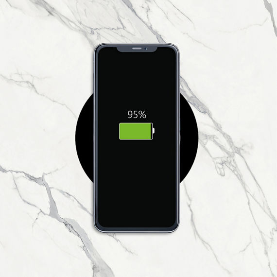 Phone charging wirelessly through a white marble look porcelain slab countertop with invisacook.