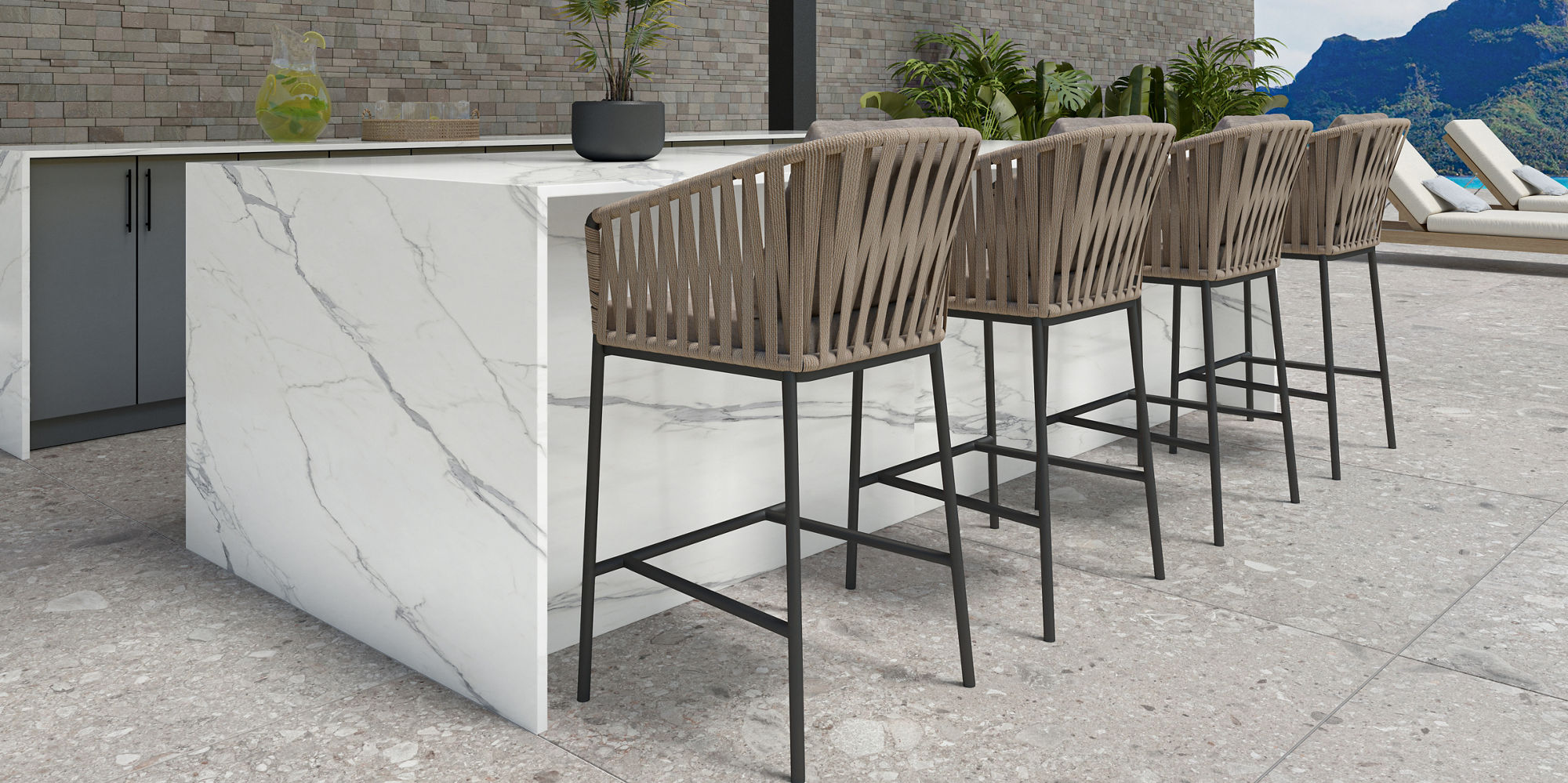Outdoor bar with wooden sitting stools, white marble look porcelain counter, and a mountain in the background.