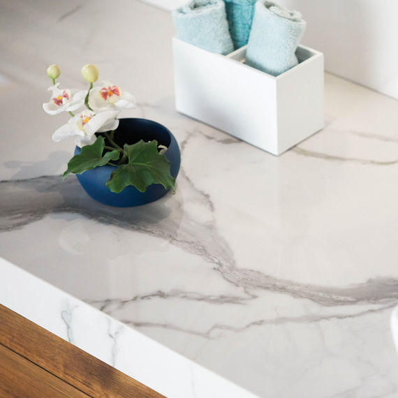 Closeup of bathroom vanity with white marble look porcelain slab countertop on natural wood cabinet and white hibiscus in blue pot.