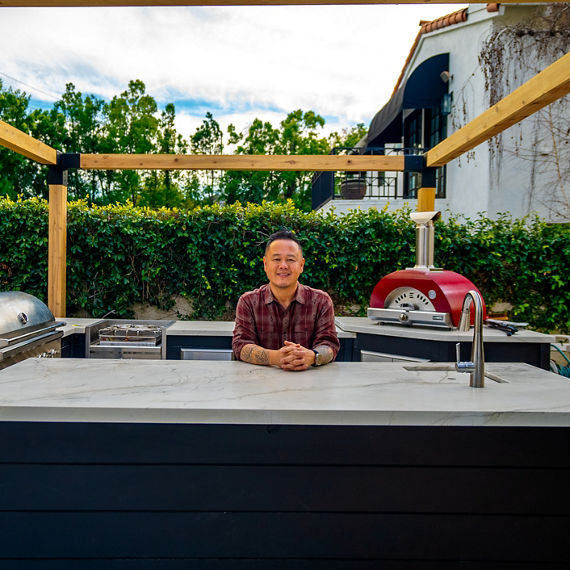 Jet Tila leaning on the outdoor kitchen island with a beige quartzite countertop.