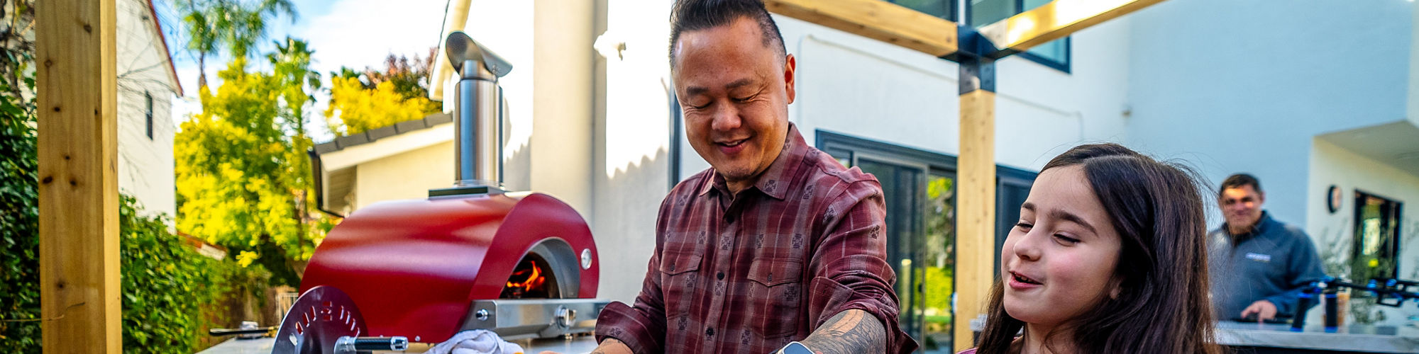 Jet Tila and a little girl preparing a pizza in an outdoor kitchen on a beige quartzite countertop.