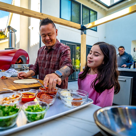 Jet Tila and a little girl preparing a pizza in an outdoor kitchen on a beige quartzite countertop.