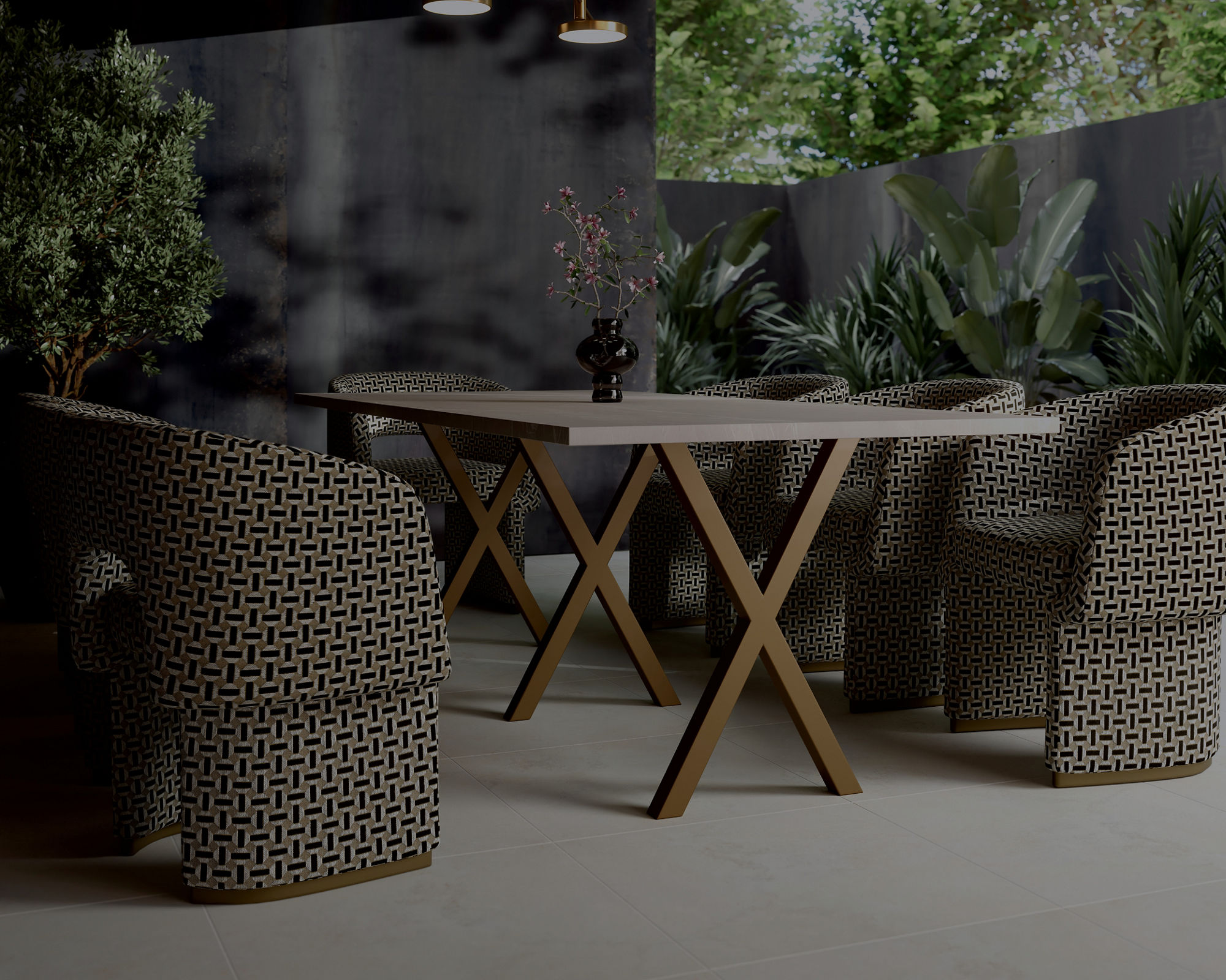 A contemporary outdoor dining space features a round table surrounded by patterned woven chairs. The setting is under a covered patio with a wooden ceiling and a modern pendant light fixture. Lush green plants and trees frame the background, adding a